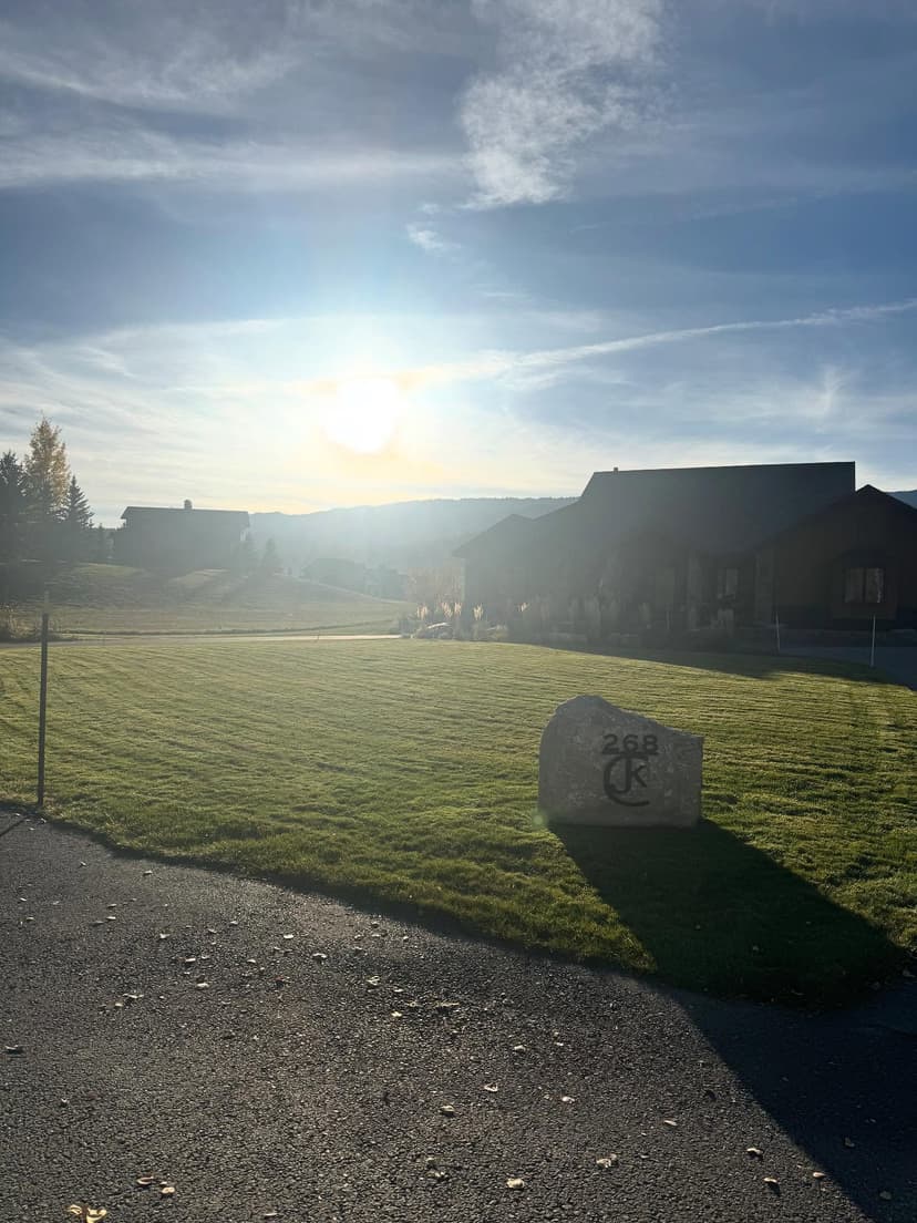 Sunrise over a grassy landscape with a stone marker, showcasing peaceful rural scenery.